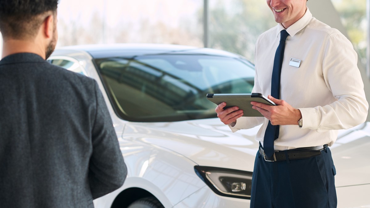 vendedor na frente de carro com tablet na mão